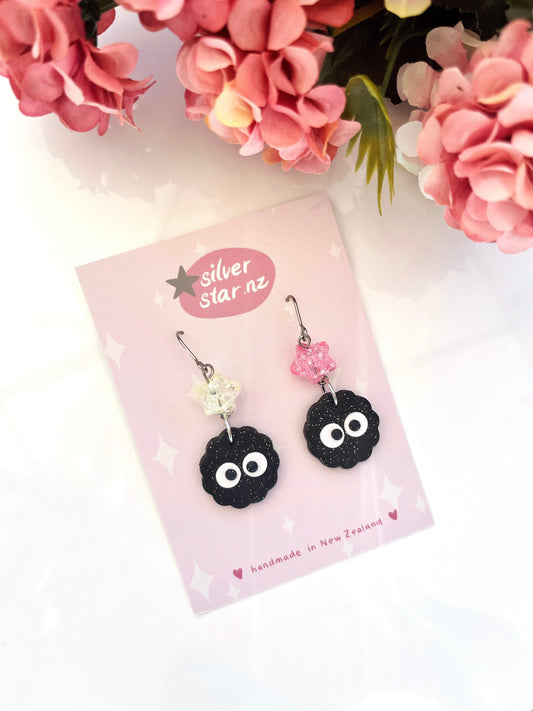 Soot Star Polymer Clay Earrings with Bead by silverstar.nz feature black soot sprite charms and glass beads on stainless steel hooks, presented on a pink card and accented by pink and white artificial flowers.