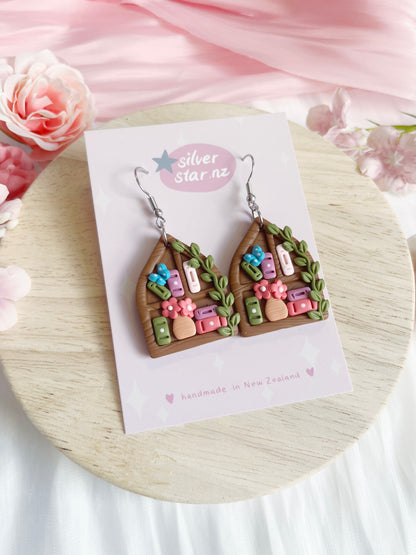 Pointed Arch Bookshelf Polymer Clay Earrings by silverstar.nz, displayed on a branded card with pink flowers on a light wooden surface. Features colorful details and stainless steel hooks.