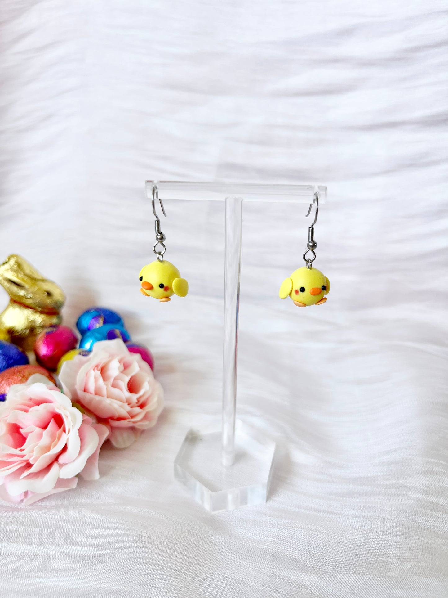 The Mini Baby Chick Polymer Clay Earrings by silverstar.nz radiate handmade charm, displayed against a white textured background with soft pink roses, colorful Easter eggs, and a small golden bunny figurine.