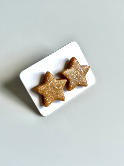 The Gold Star Polymer Clay Stud Earrings by silverstar.nz sparkle with elegance, featuring star-shaped gold designs crafted from polymer clay and durable stainless steel hooks, displayed on a white card against a light gray background.