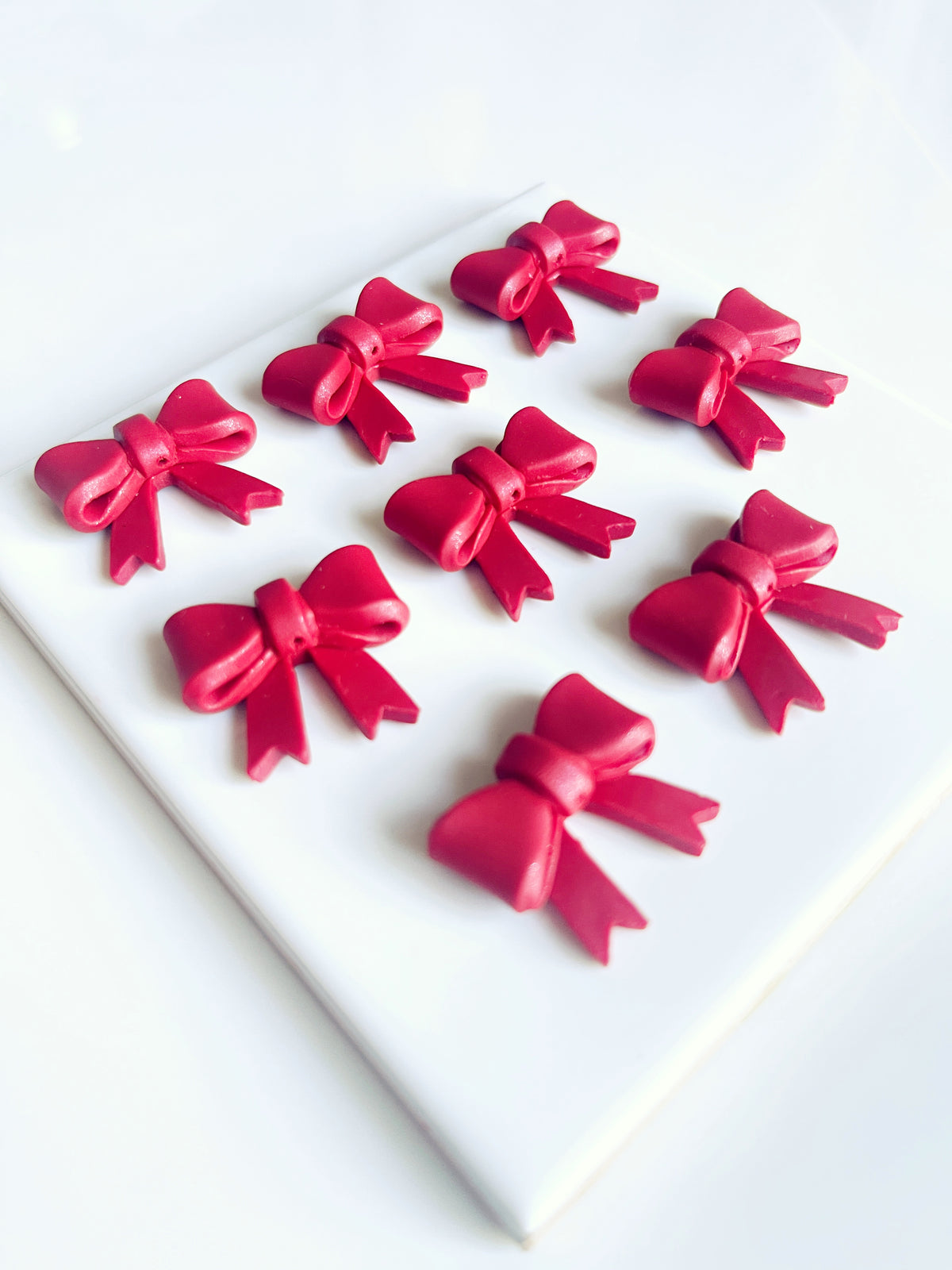 A set of nine Red Bow Polymer Clay Earrings from silverstar.nz, arranged in a 3x3 grid on a white square surface, showcases precision craftsmanship. The uniform red bows beautifully contrast against the clean background.