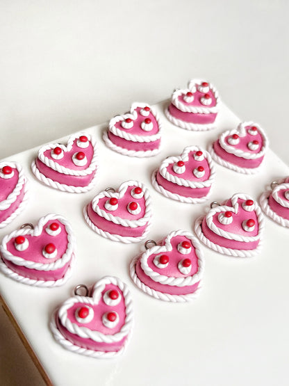 The Vintage Heart Cake Polymer Clay Earrings by silverstar.nz feature heart-shaped charms with pink and white designs on a white surface. Decorated with small white dots and twin stripes, they resemble miniature cakes and dangle elegantly from handmade stainless steel hooks.